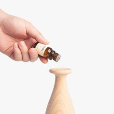 a hand is holding an essential oil bottle in front of a small wooden stopper