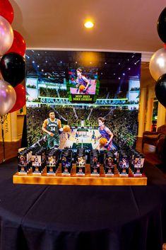 a table topped with photos and balloons in front of a large screen displaying basketball players