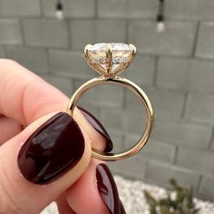 a hand holding a ring with a diamond on it's side and a brick wall in the background