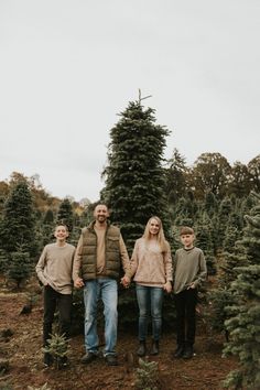 three people standing in front of a christmas tree at the farm with their hands on each other's shoulders