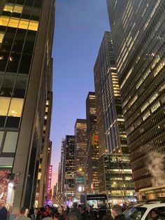 many people are walking on the sidewalk in front of tall buildings at night with bright lights