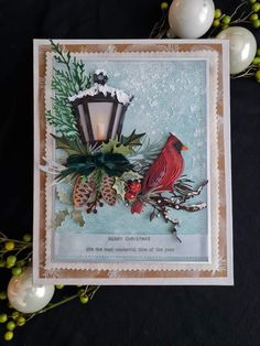 a christmas card with a cardinal sitting on top of pine cones and greenery next to a lit candle