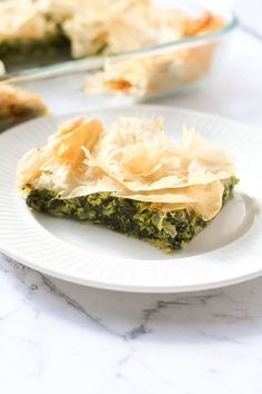 a slice of quiche with spinach and cheese on a white plate next to a casserole dish