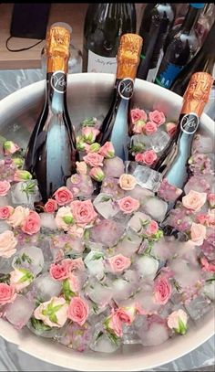 four bottles of champagne are in an ice bucket with pink flowers and roses on it