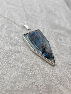 This beautiful handmade, one-of-a-kind silver pendant with a real Blue Apatite Stone accent is perfect for dressing up or down. This pendant has approximately a height of 2 in. x 1 in. in length and is made from a durable silver metal alloy, and stone set in blue mica tinted resin. Unique Blue Sterling Silver Jewelry, Unique Silver Jewelry For Memorial, Unique Silver Jewelry For Remembrance, Unique Blue Jewelry With Large Pendant, Blue Necklace With Large Rectangular Pendant, Blue Labradorite Jewelry With Large Stone, Blue Teardrop Pendant Jewelry With Large Stone, Blue Metal Amulet Jewelry, Blue Rectangular Pendant Necklace