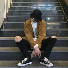 a young man sitting on the steps with his hands in his pockets and wearing sneakers