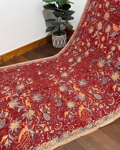 a large red blanket sitting on top of a wooden floor next to a potted plant