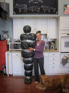 a woman standing next to a statue in a kitchen with a dog laying on the floor