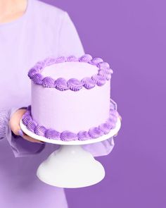 a woman holding a cake with purple icing on it