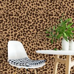 a leopard print wallpaper with a white table and chair in front of it, next to a potted plant