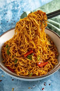 a bowl of noodles with chopsticks in it on a blue and white table cloth