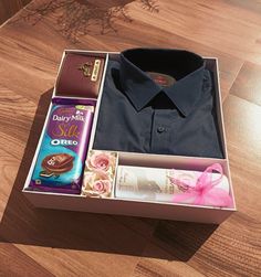 an open box with some items inside it on a wooden floor and a pink ribbon