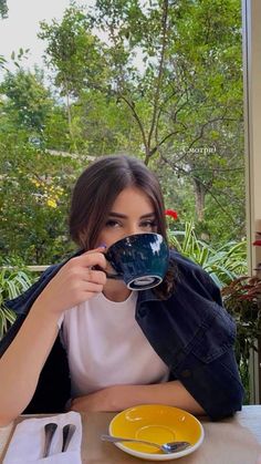 a woman sitting at a table with a plate and cup in front of her face