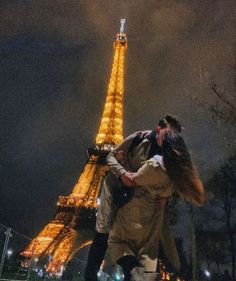 a man and woman kissing in front of the eiffel tower, at night