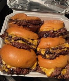 four cheeseburger sandwiches in a take out container with aluminum foil on the side