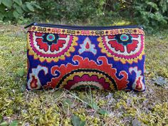 a colorful purse sitting on top of a grass covered field next to trees and bushes