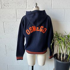 "This 1940-1950's vintage Champion hoodie is made from a navy blue, fleeced nylon with  orange and blue striped ribbed knit waistband and sleeve cuffs. Represents the Oswego High School Panthers track team of  Oswego, Illinois across the back and the number 138 on the left sleeve. Zips up with a Talon teardrop zipper. In excellent vintage condition with no signs of wear. Marked a size M, see below for measurements 19\" shoulders 40\" chest 25\" length 24\" sleeve length" Navy Vintage Long Sleeve Outerwear, Navy Long Sleeve Sweatshirt Sportswear, Navy Long Sleeve Sportswear Sweatshirt, Vintage Blue Sweatshirt For Sports, Vintage Navy Long-sleeve Outerwear, Orange Fleece, Track Team, Vintage Champion, Champion Hoodie