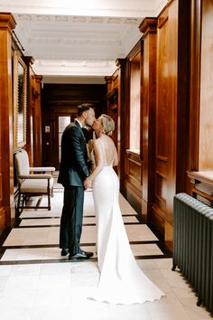 a bride and groom are standing in the hallway at their wedding reception, with wood paneling on the walls behind them