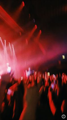 a crowd of people at a concert with their hands in the air and lights on