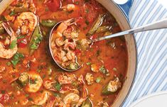 a pot filled with shrimp and vegetable soup on top of a blue striped table cloth