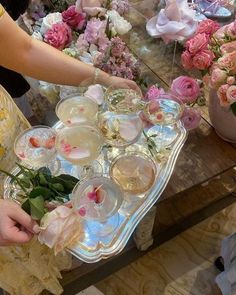 a woman is holding a tray full of flowers and glasses with water in them on a table