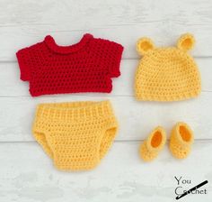 crocheted baby clothes and booties are laid out on a white wooden surface