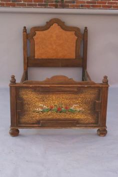 an antique wooden bed frame with hand painted flowers and leaves on the side, in front of a brick wall