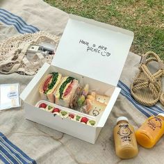 an open box with sandwiches and juice on a blanket