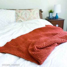 an orange knitted blanket on top of a bed next to a night stand and nightstand