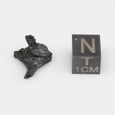 a small piece of metal sitting next to a black cube with the letter n on it