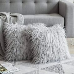 two fluffy pillows sitting on top of a rug next to a gray couch and coffee table