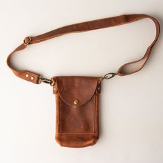 All leather belt bag with adjustable, removable belt strap, phone pocket, interior credit card/ID card pocket, and snap closure.  Perfect for keeping things to a minimum - phone, keys, cash, and a couple of cards.   SIZE 8" high x 5" wide x 1 3/4" deep Detachable & Adjustable Belt Strap: 1" wide Will fit waist measurements from 30 inches to 54 inches. MATERIALS Genuine Kodiak Leather Antique brass hardware Interior leather pocket ONE OF A KIND Leather is natural and unique, adding character & making each product imperfectly beautiful. Each piece is a handcrafted one-of-a-kind piece. The bag you receive will differ from the photograph, but we will ensure that yours is just as beautiful. ABOUT US Frankie & Co. is a leather goods brand focused on quality and craftsmanship. Our products are ha Brown Belt Bag With Cell Phone Pocket For Everyday, Functional Brown Leather Phone Bag, Leather Wallet With Cell Phone Pocket For Everyday, Brown Crossbody Belt Bag With Cell Phone Pocket, Everyday Carry Crossbody Belt Bag For Mobile Phone, Functional Brown Phone Bag For Everyday Use, Leather Belt Bag With Belt Clip For Travel, Brown Belt Bag With Belt Clip For Daily Use, Functional Brown Pouch Phone Bag