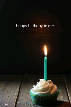 a cupcake with a lit candle sitting on top of a wooden table in front of a dark background