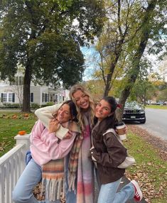 three girls are posing for the camera in front of a white picket fence and trees