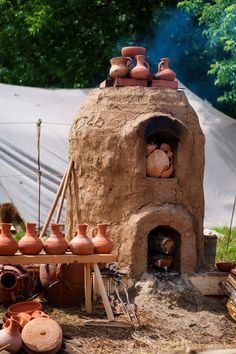 an outdoor oven made out of clay with pots on it's sides and other items around