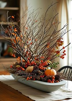 a bowl filled with branches and pumpkins on top of a table