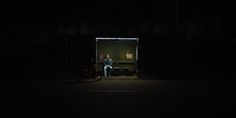 a man sitting on a bench in the dark next to a bike and a container