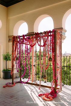 an outdoor ceremony with pink and red garlands on the fence, hanging from arches