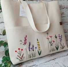 a bag with flowers painted on it sitting against a white brick wall next to green plants