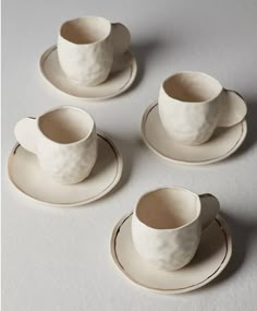 four white cups and saucers sitting next to each other on top of a table