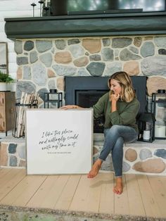 a woman sitting in front of a fireplace holding a sign