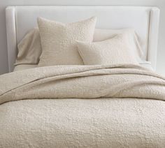 a white bed with two pillows on top of it and a blanket over the headboard