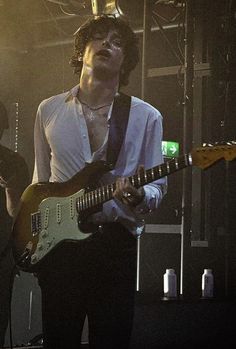 the man is playing his guitar while standing on stage with other people in the background