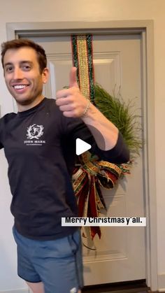 a man giving the thumbs up sign in front of a door with christmas decorations on it