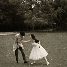 a man and woman are dancing in a field together, with trees in the background