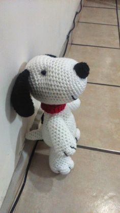 a crocheted stuffed dog with a red collar on it's neck standing next to a wall