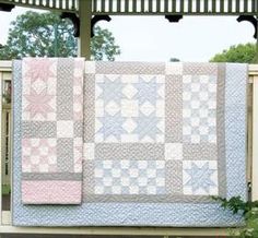 a quilt hanging on a fence in front of some trees and bushes with an arbor behind it