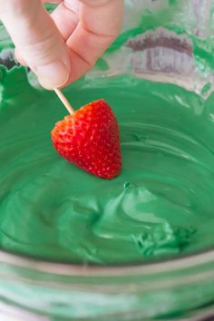 a person dipping a strawberry into green liquid in a glass bowl with a toothpick