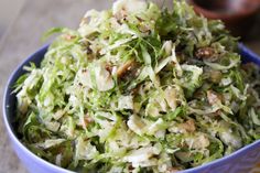 a blue bowl filled with shaved lettuce next to a brown and white plate