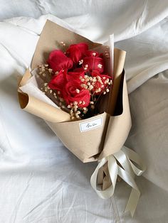 a bouquet of red flowers in a brown paper wrapped box on a white bed sheet